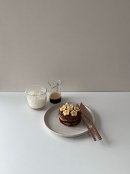 Aesthetic minimalist setup featuring banana pancakes with coffee and cream.