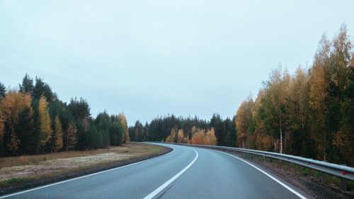 Free Curved road winds through a peaceful autumn forest with colorful foliage under a clear sky. Stock Photo