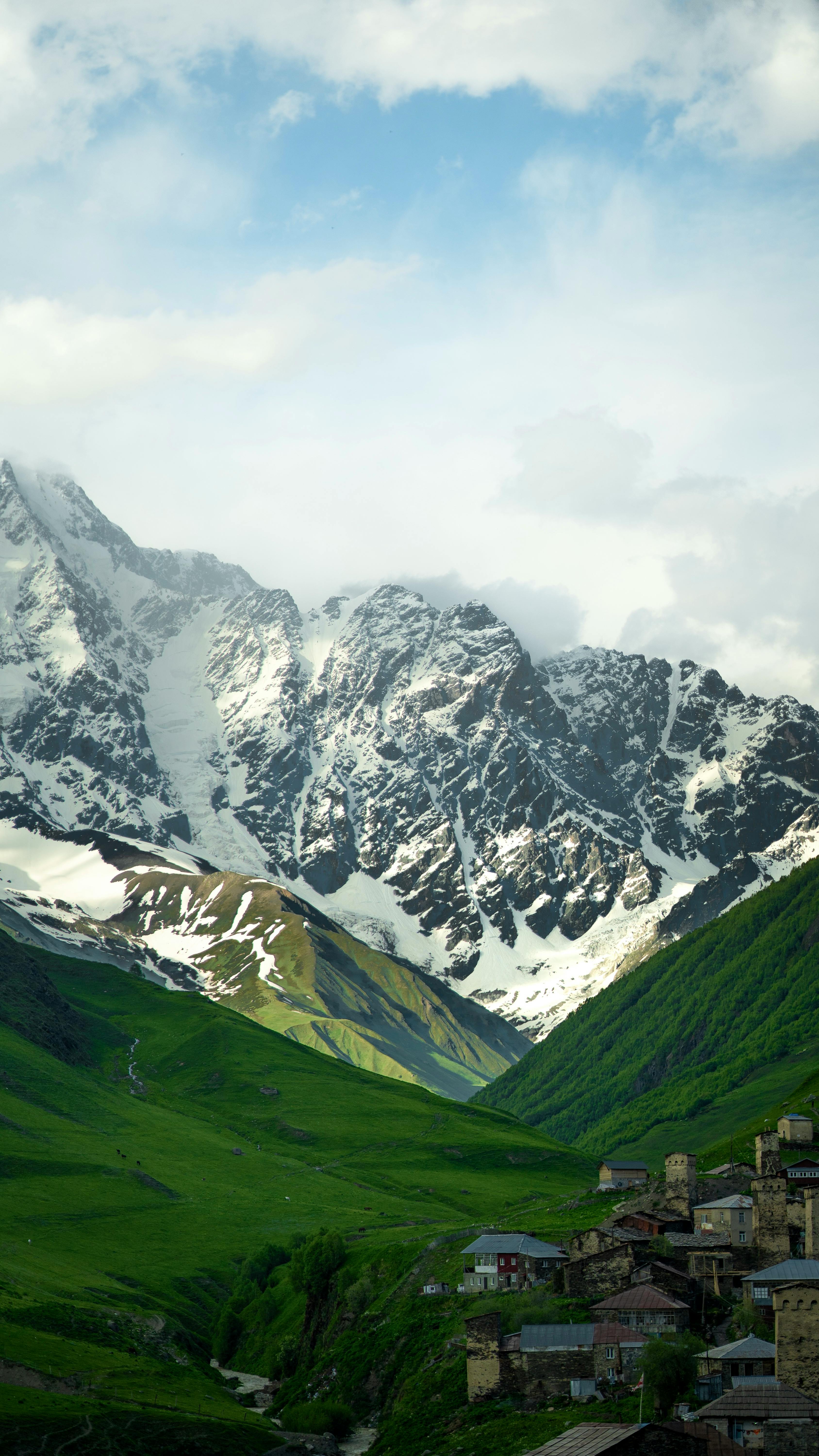 Idyllic mountain village nestled below snow-covered peaks with lush green valleys.