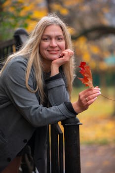 在公园里，一位金发女子正手持红色秋叶的肖像