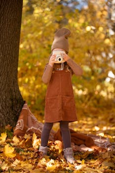 A young girl in autumn attire photographs a vibrant forest, capturing the essence of fall.