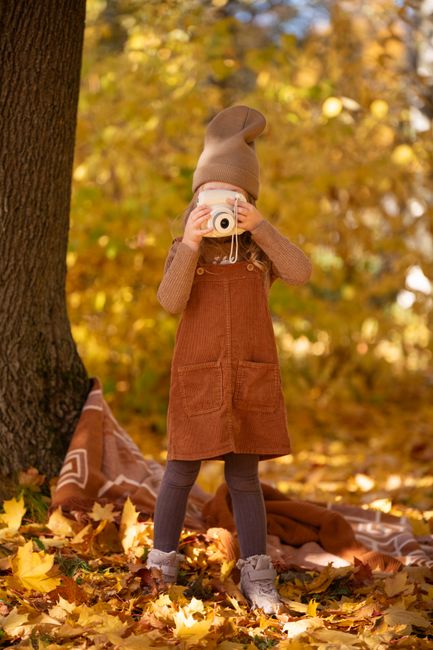 A young girl in autumn attire photographs a vibrant forest, capturing the essence of fall.