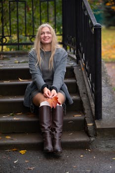 Smiling woman sitting on steps holding a red maple leaf during fall.