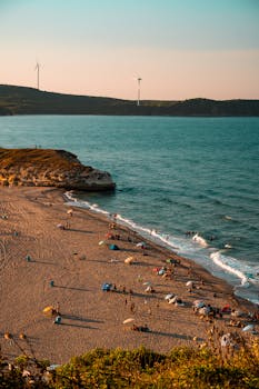 A coastal view in Kırklareli, Türkiye, featuring a busy beach and wind turbines under clear skies.