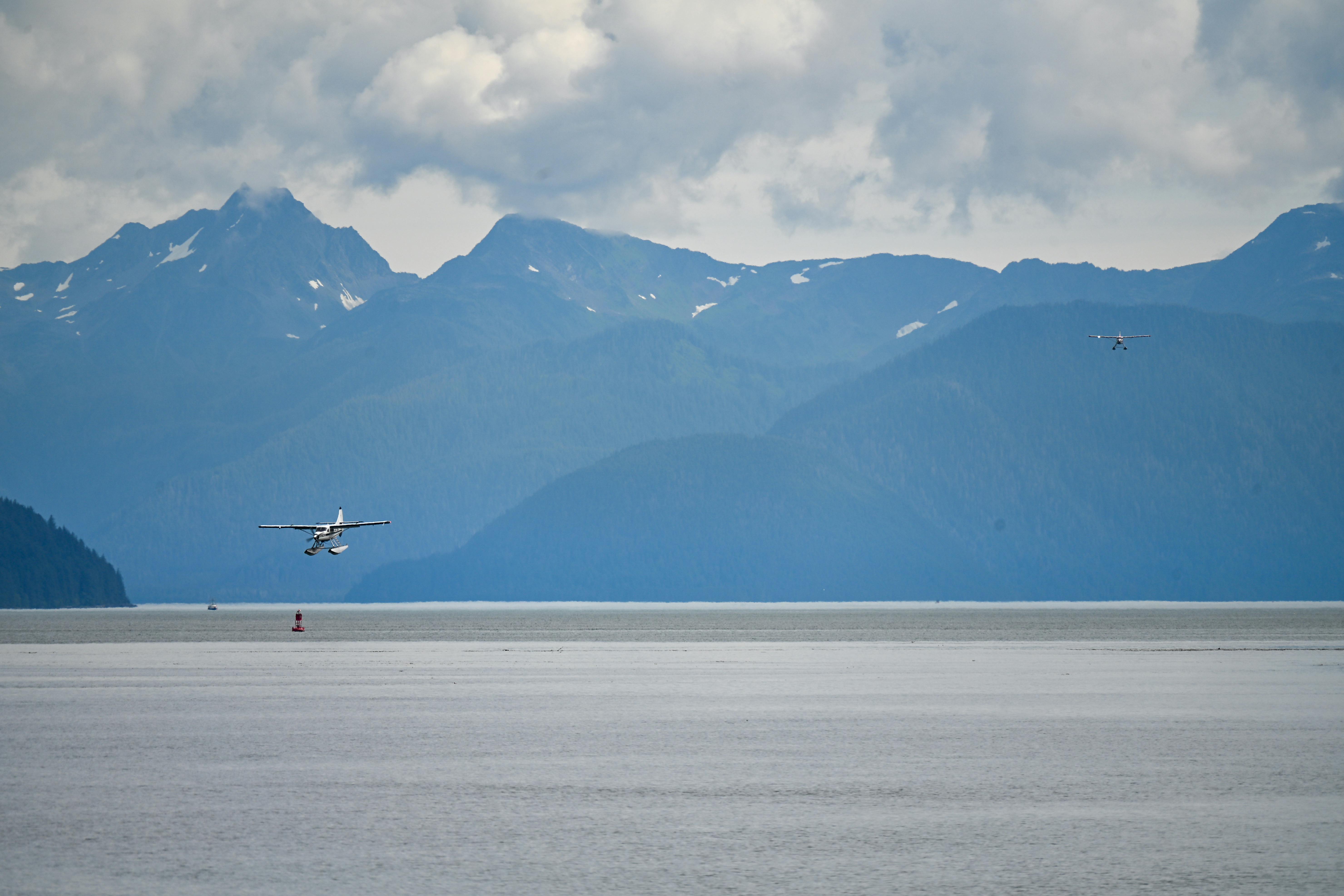 A seaplane landing in Juneau, Alaska, with majestic mountains and cloudy skies.