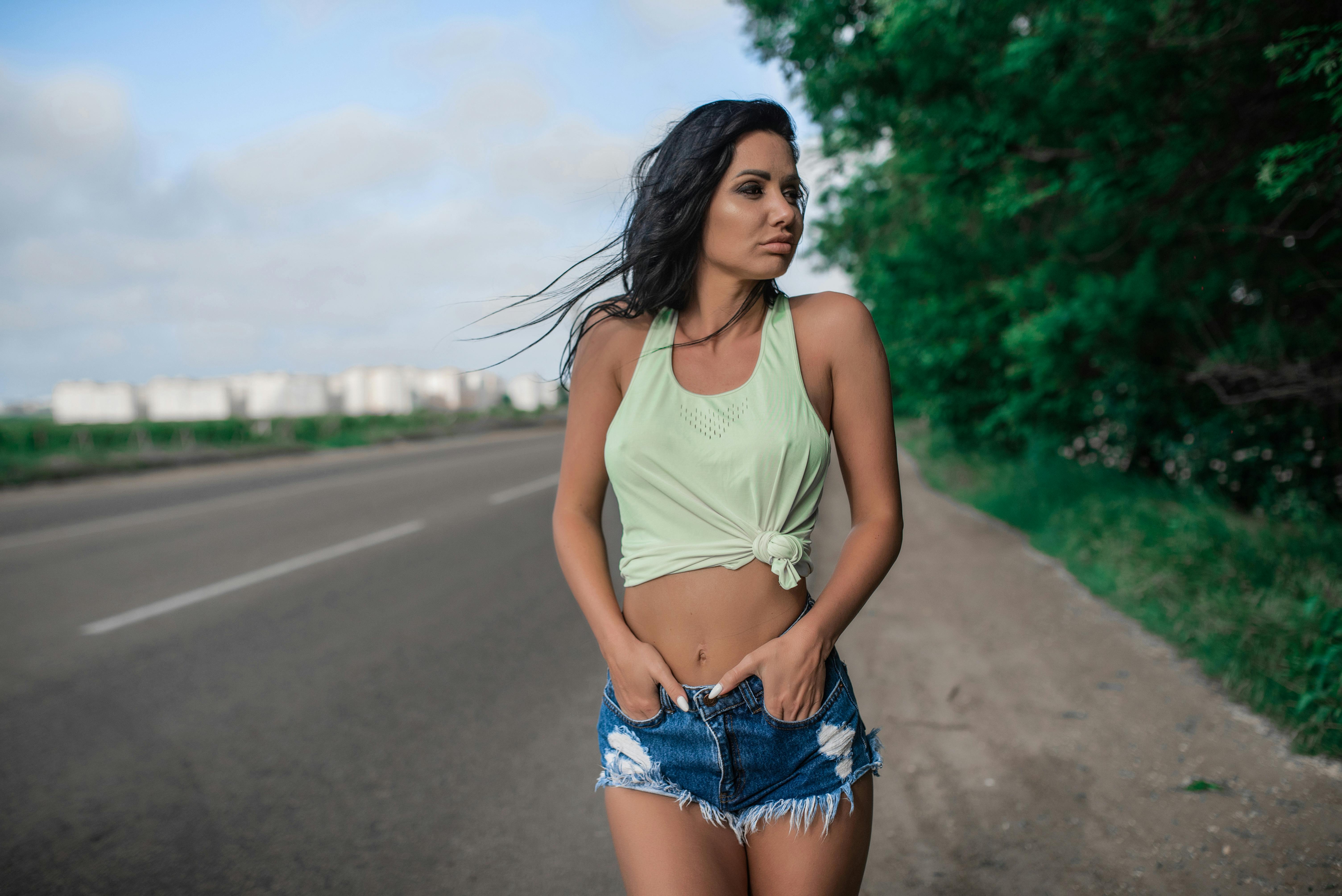 一名身穿牛仔短裤和绿色上衣的女子自信地站在路边