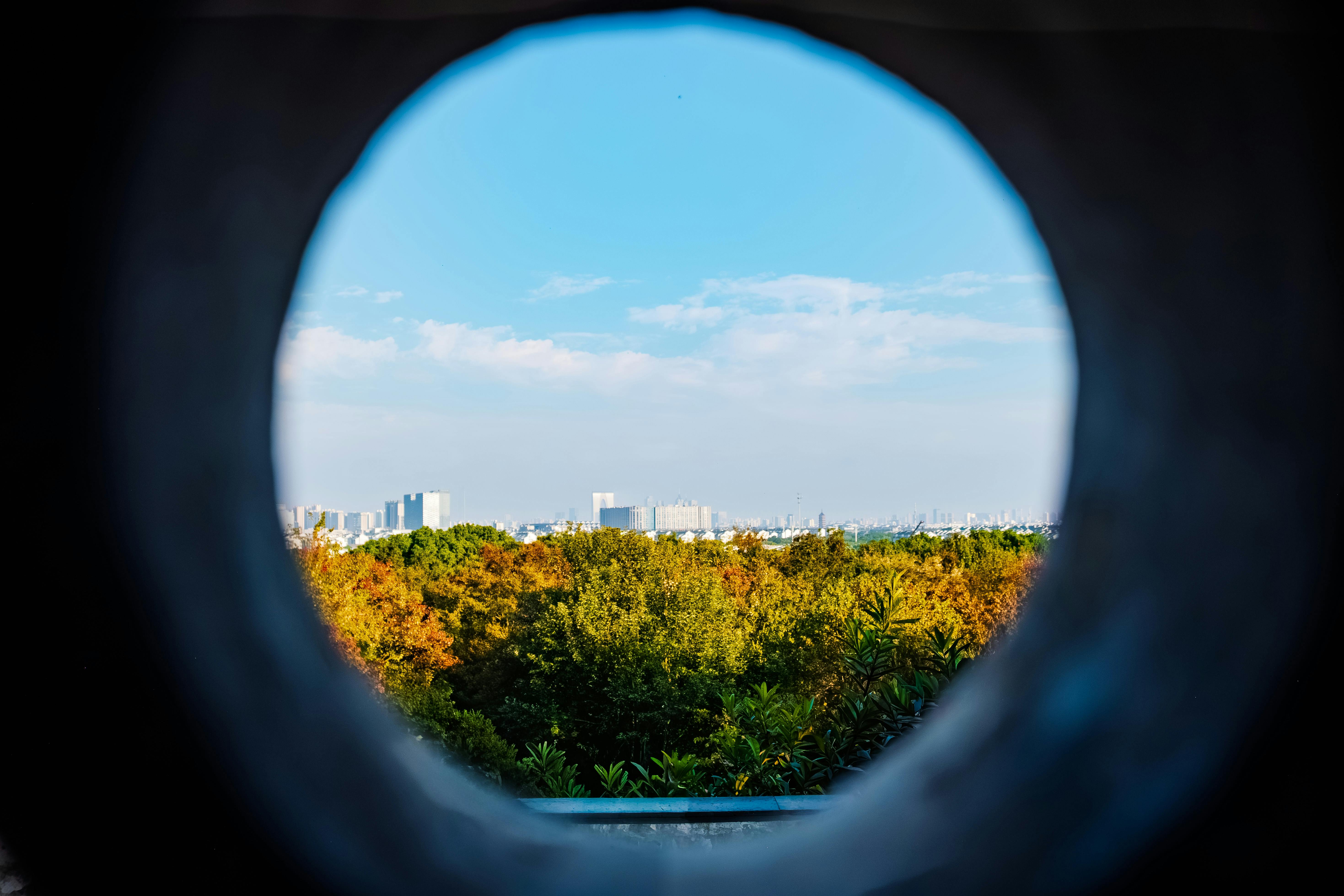 Catch a unique perspective of Suzhou cityscape viewed through a round opening, blending urban and natural landscapes.