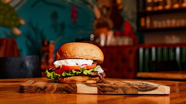 Delicious cheeseburger with fresh ingredients served on a wooden board in a cozy restaurant setting.