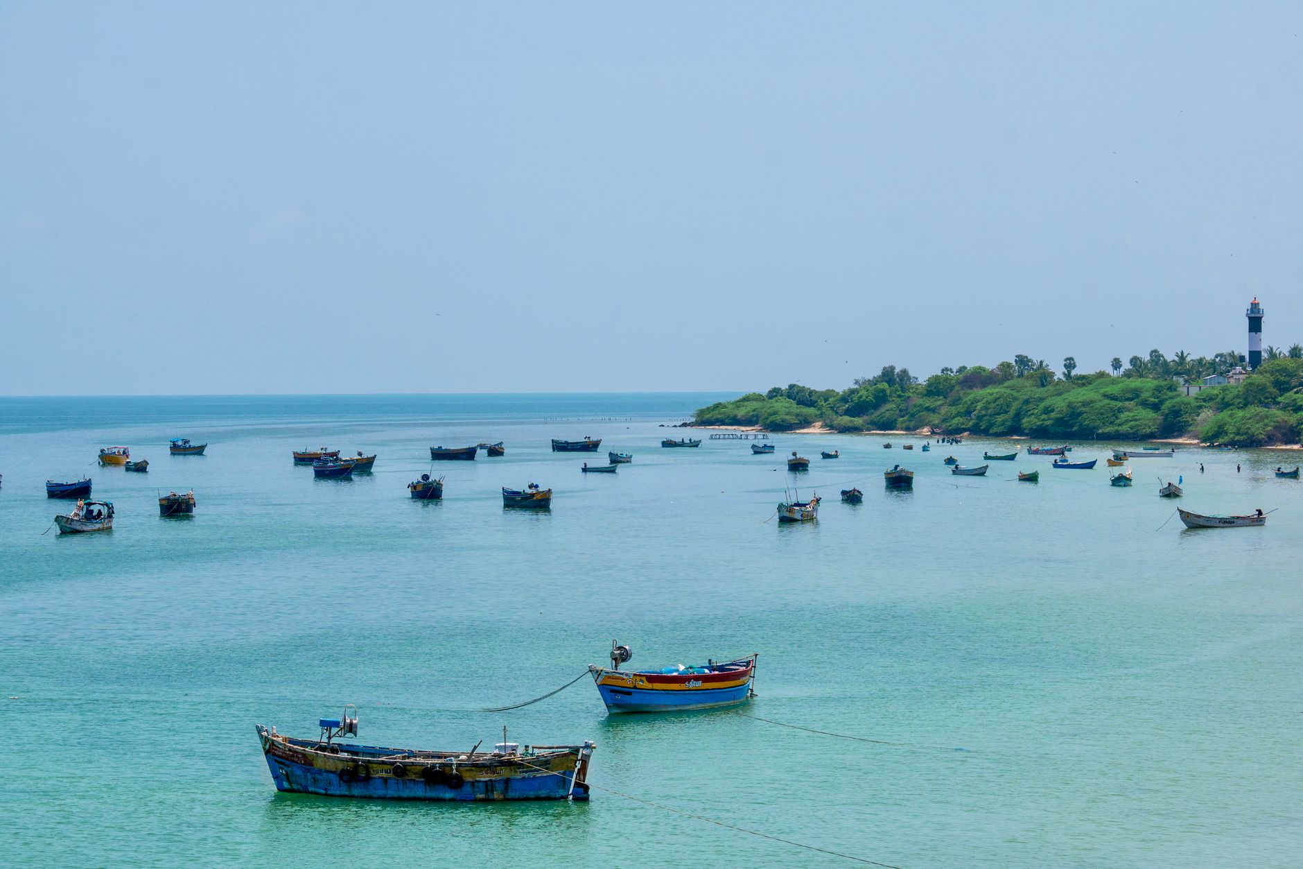 Vibrant fishing boats near Rameswaram lighthouse in Tamil Nadu, India, on a clear day.