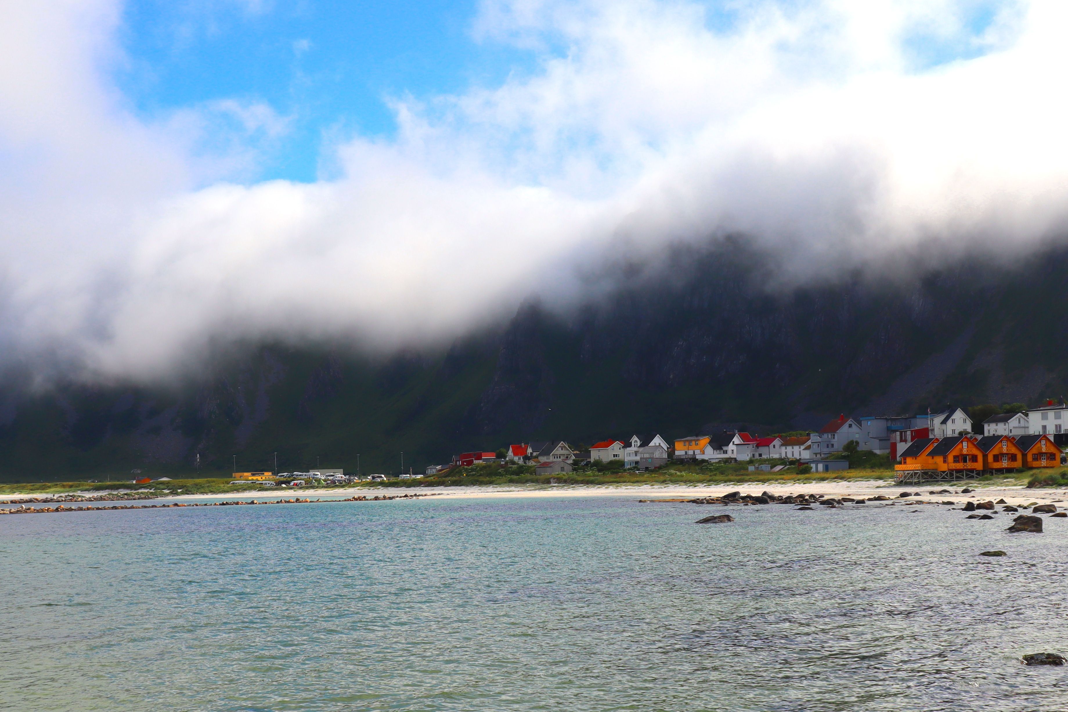 Charming coastal village with colorful houses by the sea under a dramatic cloudy sky. - Lofoten