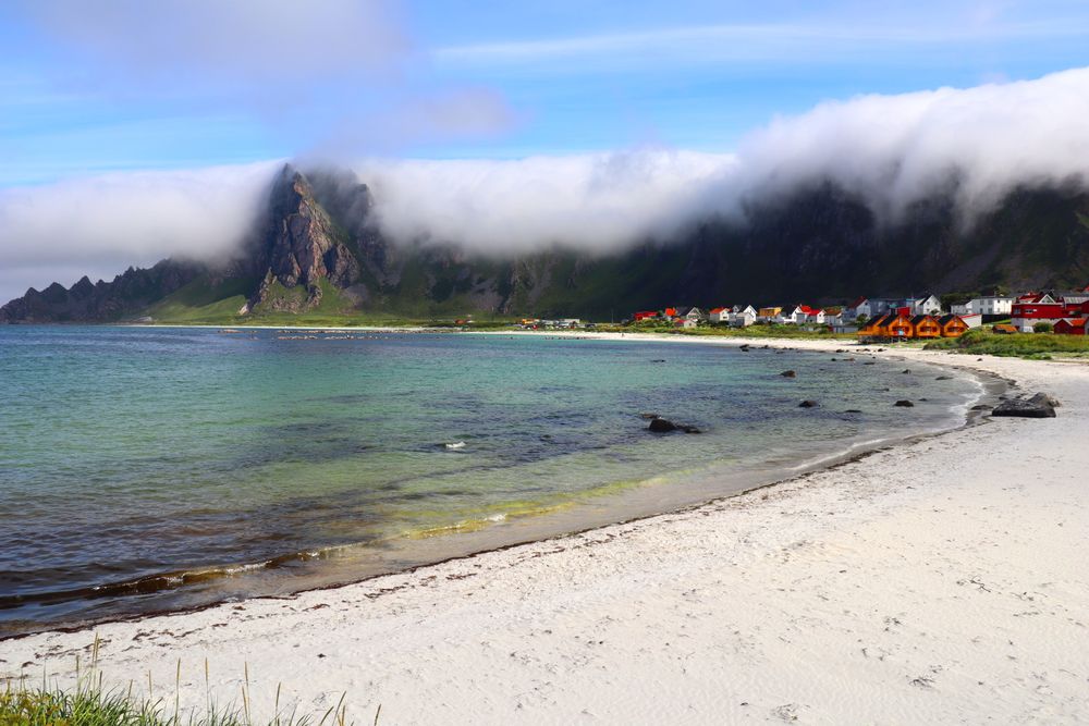 Plajă din Lofoten cu sat de coastă și munți în ceață