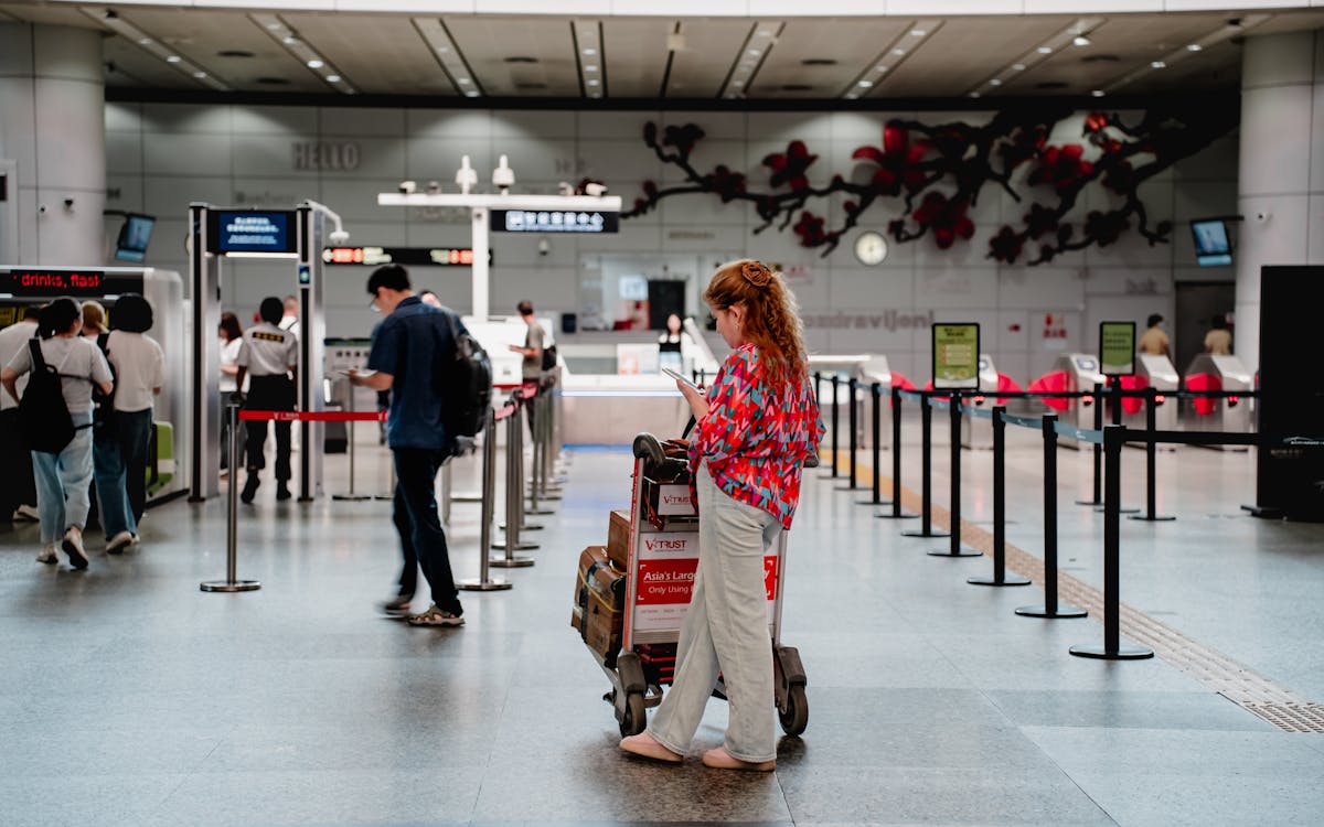 A traveler checks her phone while waiting with a luggage cart at a busy airport terminal in Guangzhou.