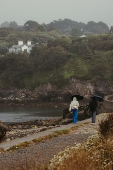 Two people walk with umbrellas on a rainy day near a coastal path in Howth, Dublin.