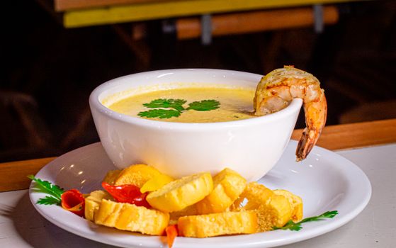 A bowl of creamy shrimp soup garnished with cilantro and served with bread slices on a plate.