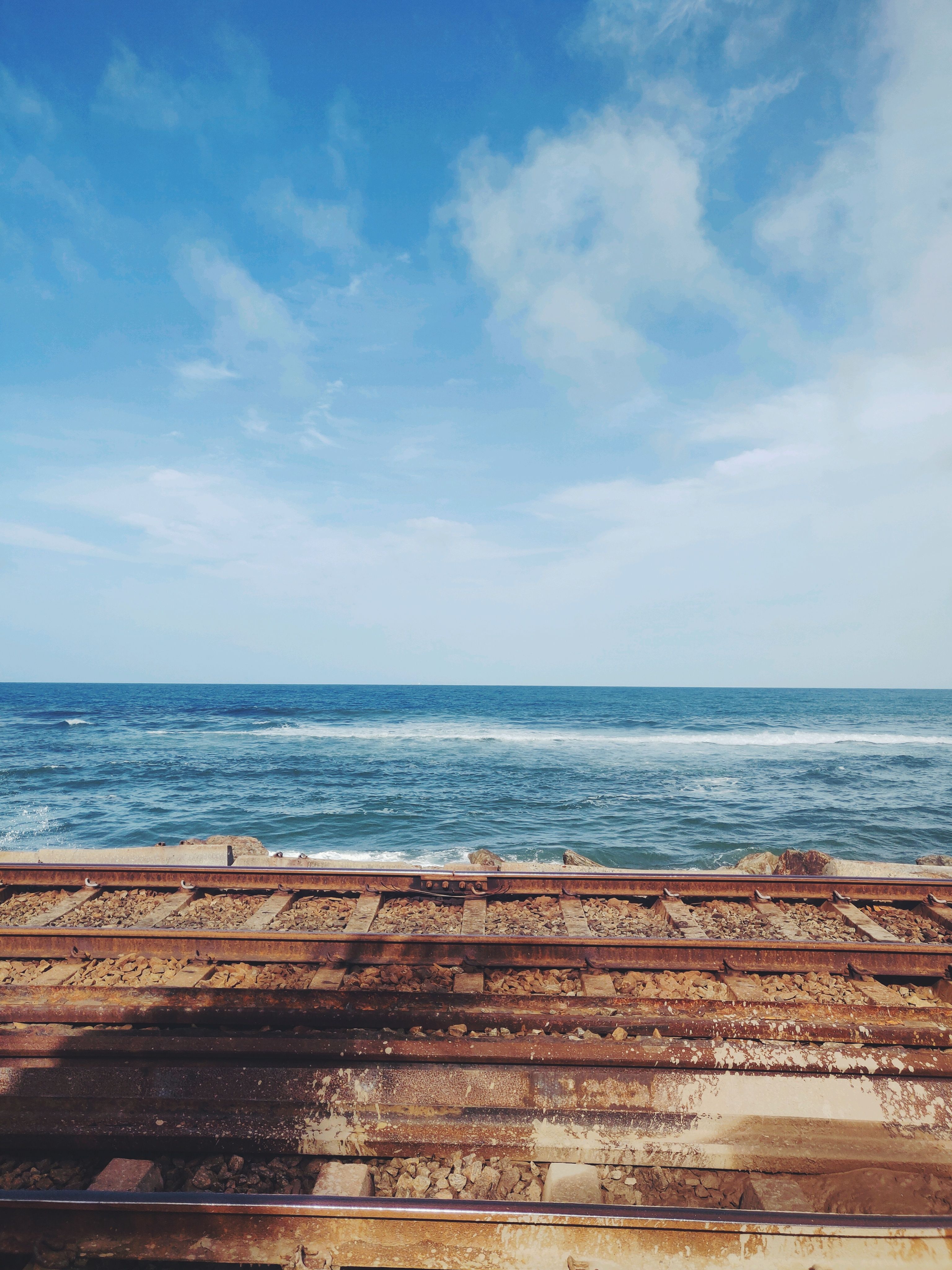 anime illustration of a girl by a coastal railway with a bright turquoise ocean and fluffy clouds