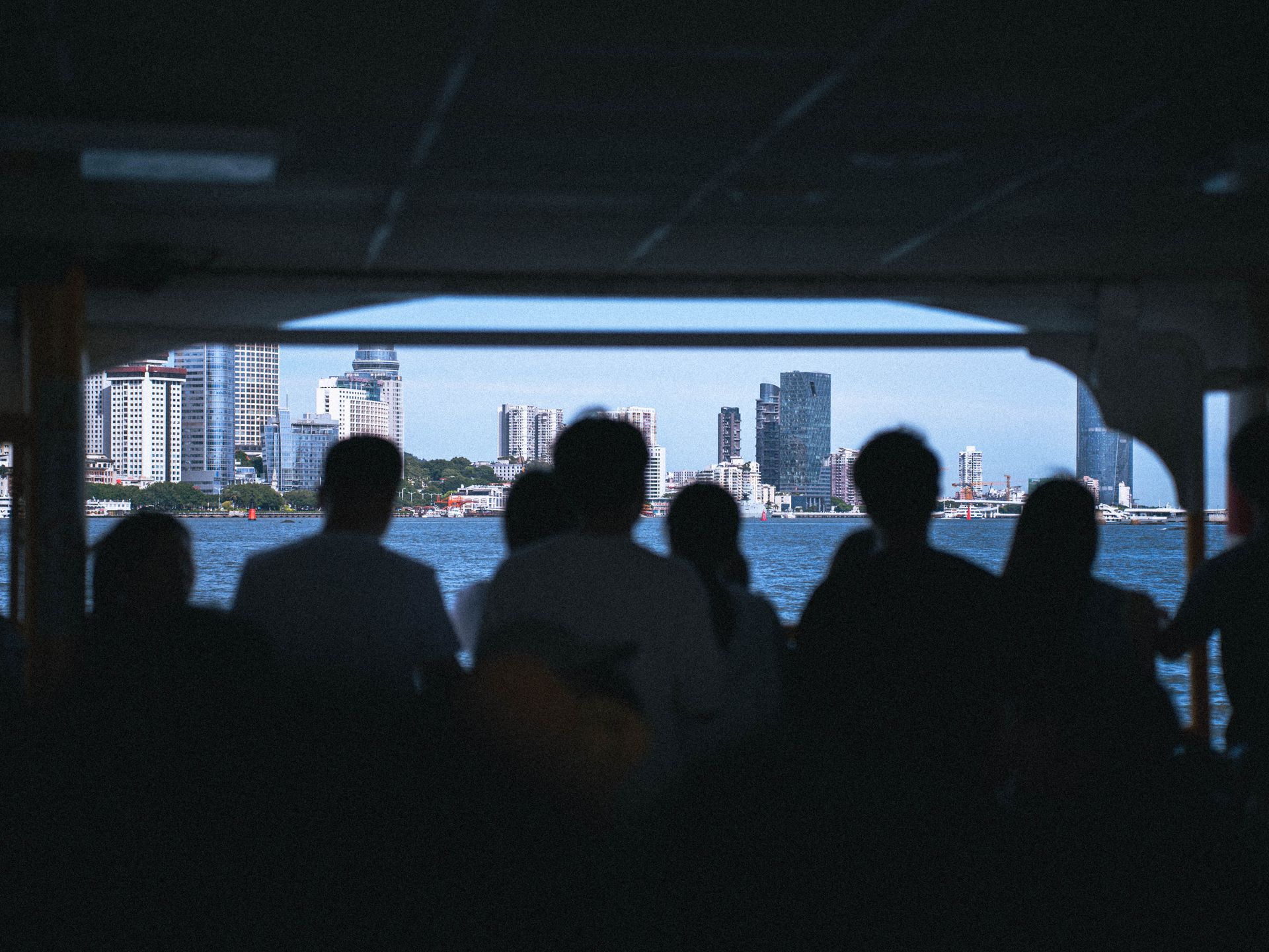 Silhouetted group viewing city skyline from ferry window, capturing urban exploration.