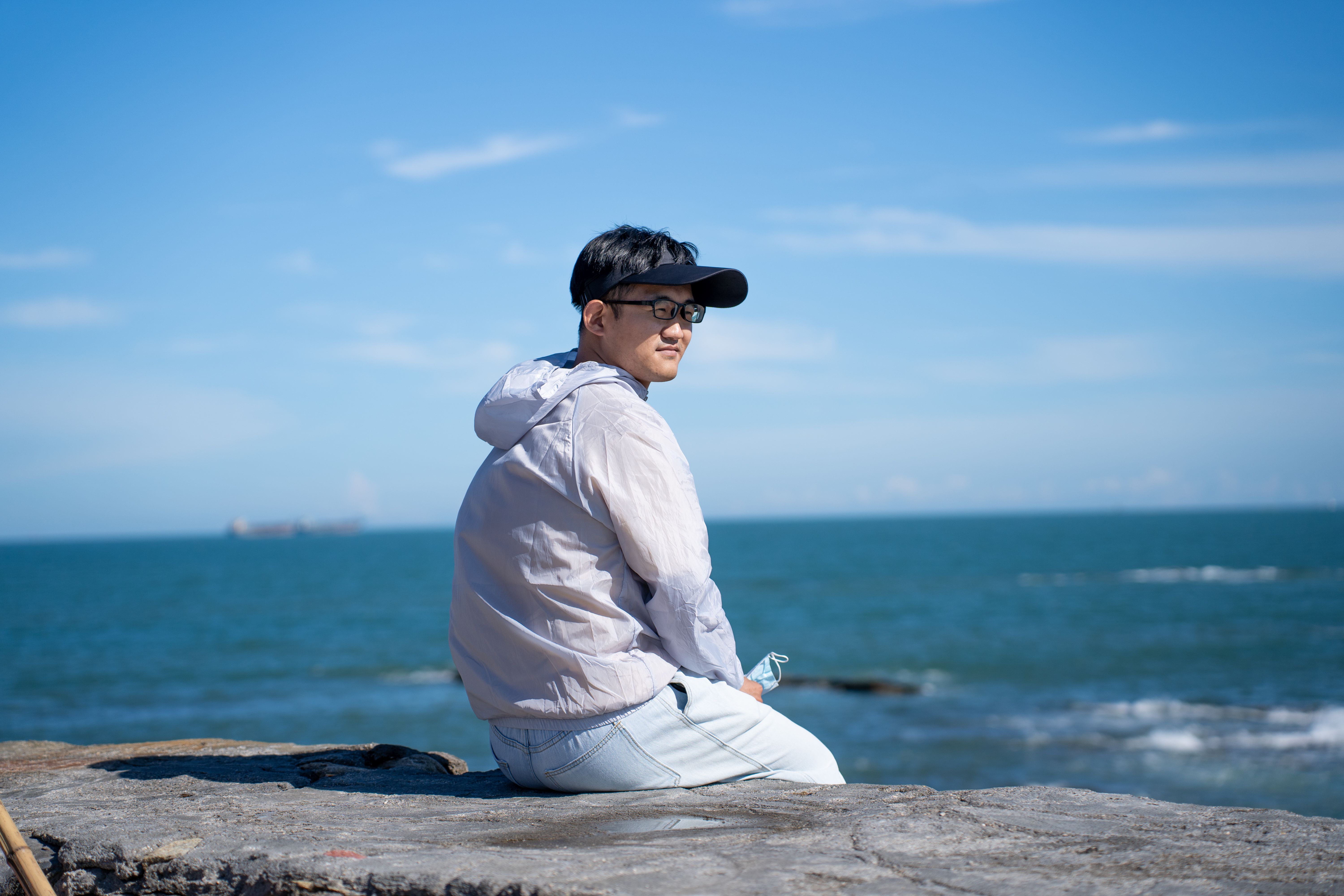 Man sitting on a rock near the sea enjoying a clear summer day with blue skies.