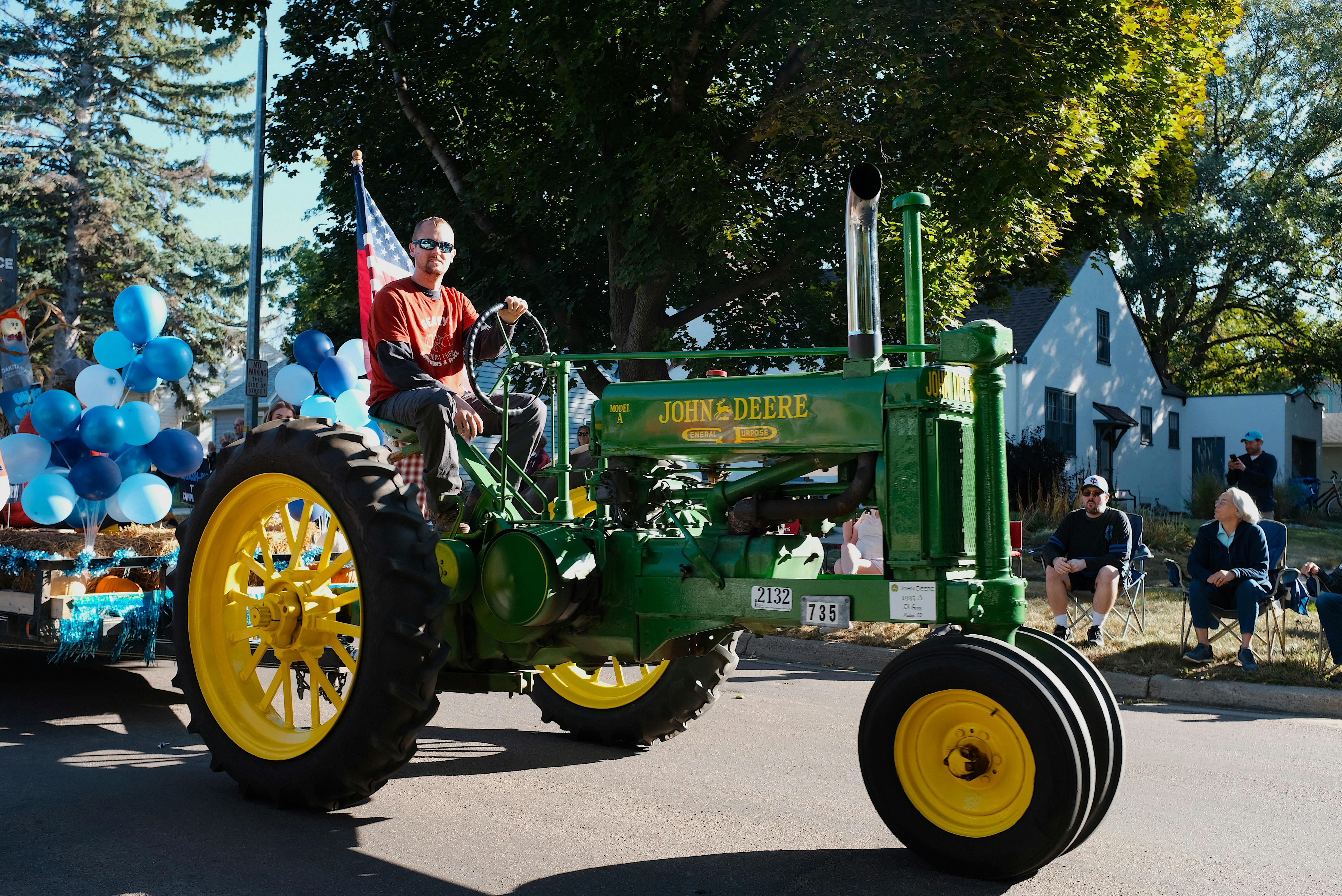 A classic John Deere Model A tractor participating in an outdoor parade with onlookers.