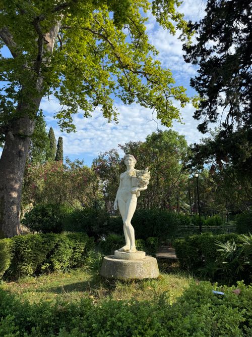Free A stone statue of a woman holding flowers standing in a vibrant garden during daytime. Stock Photo