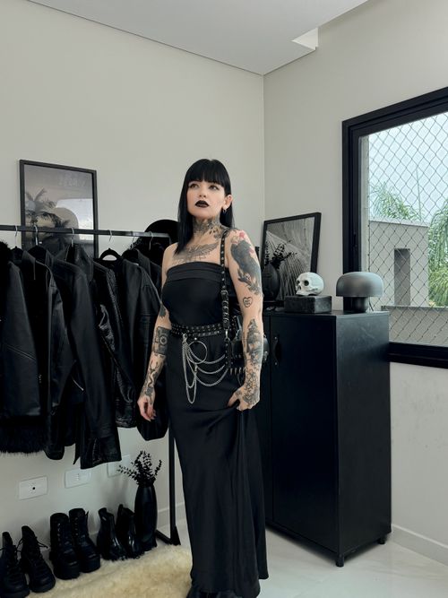 Free Tattooed goth woman in black dress surrounded by dark decor indoors. Stock Photo