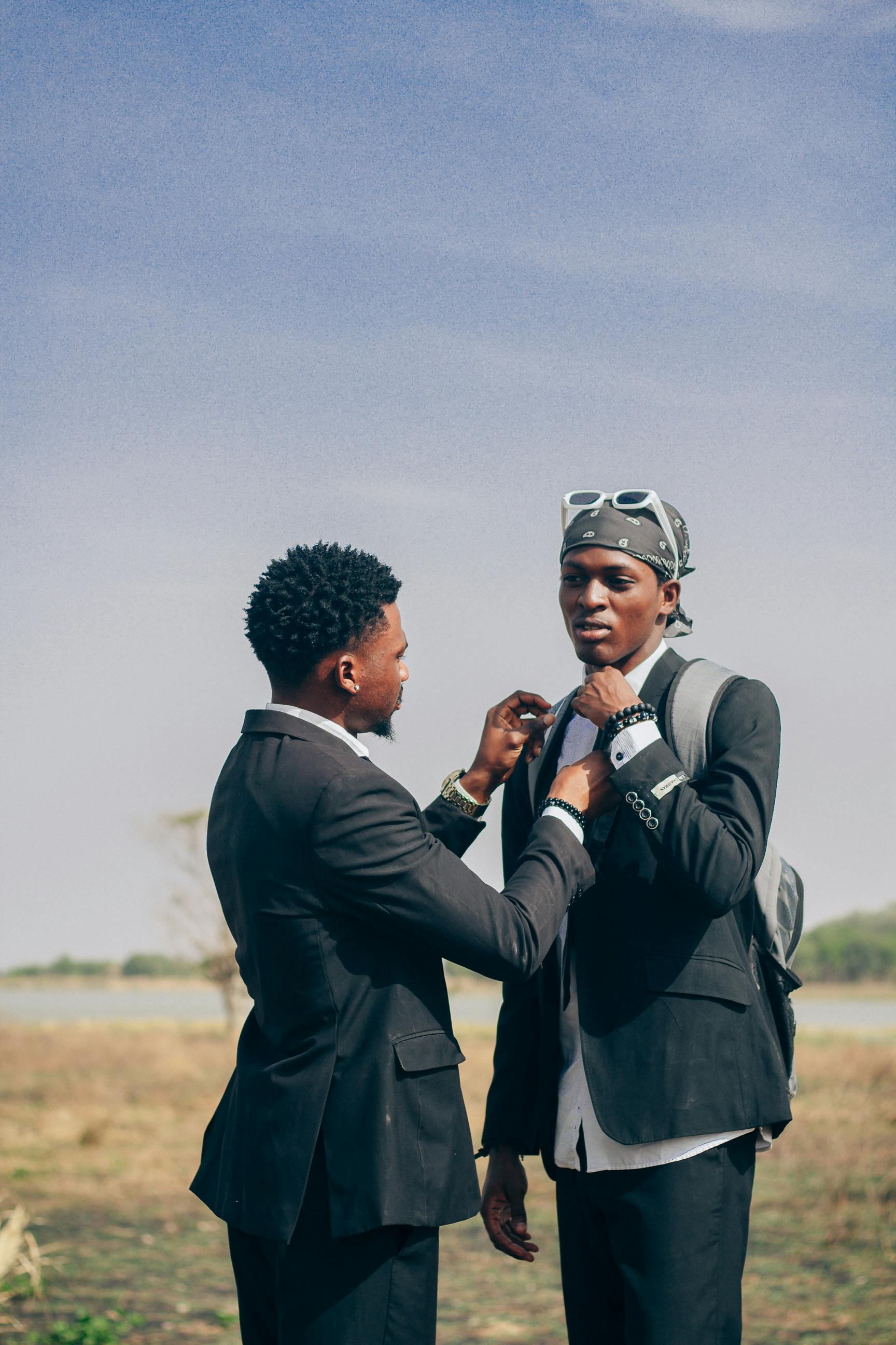Two young men in suits, engaging outdoors in Zaria, Nigeria, displaying friendship.