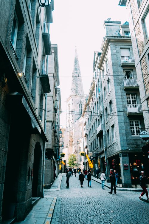Free Unrecognizable people walking on narrow paved pedestrian street near old church and buildings in ancient city district Stock Photo