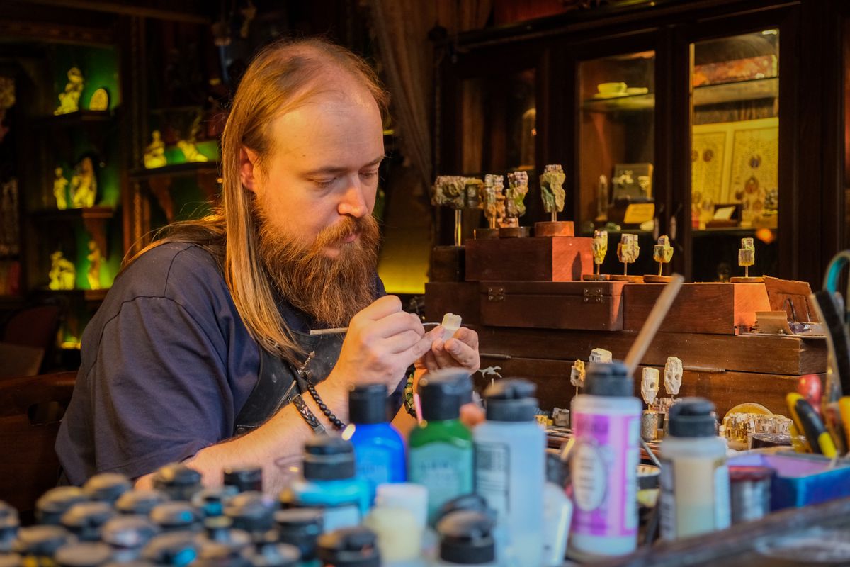 A caster working at a bench surrounded by paints, tools and small resin parts