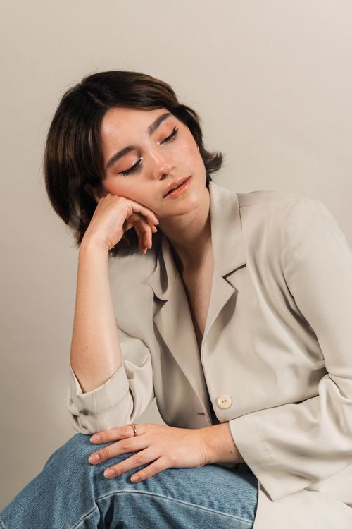 Free Elegant young woman in a beige blazer and jeans posing thoughtfully indoors. Stock Photo