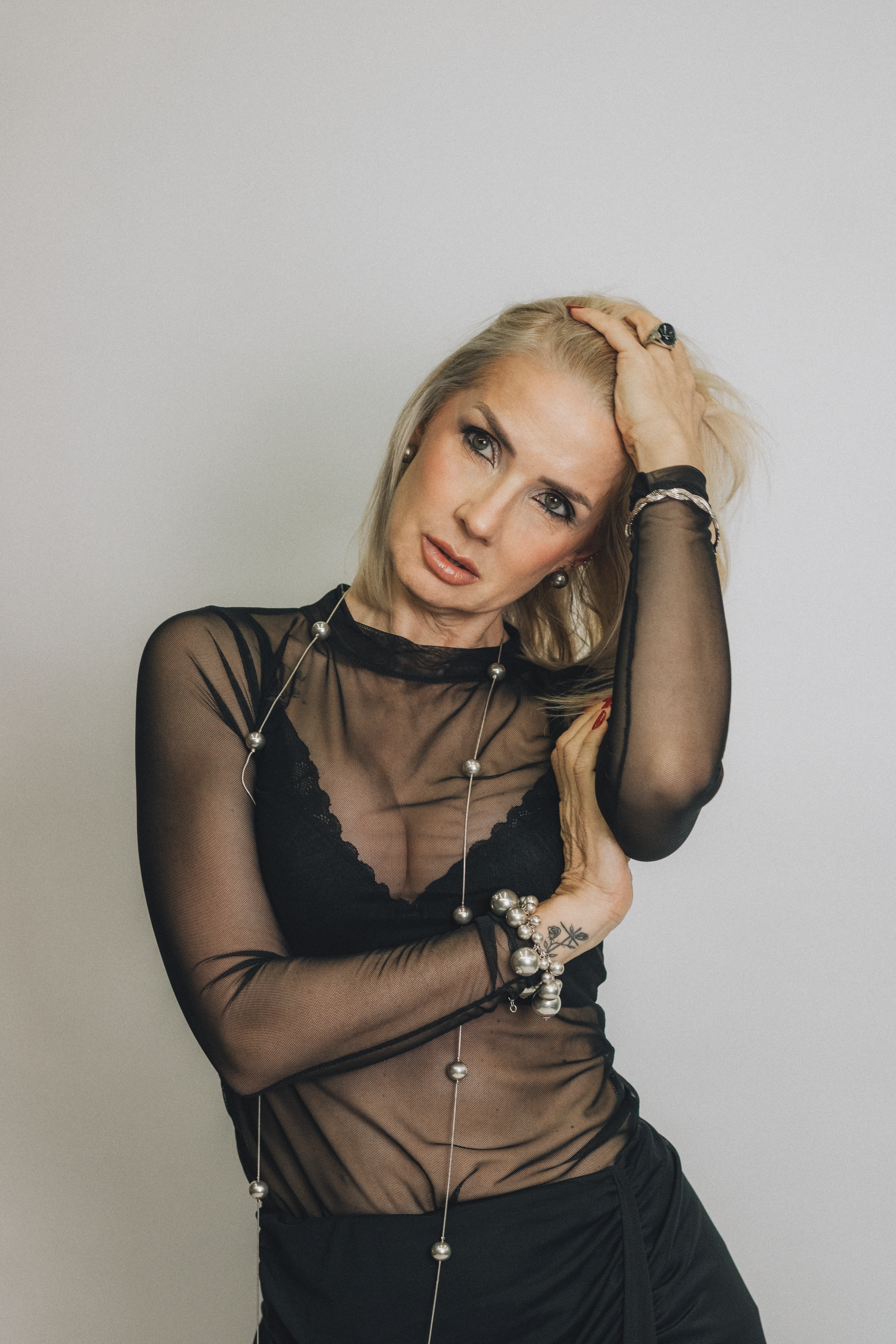 Stylish woman in modern black sheer top posing indoors, showcasing elegance and fashion.