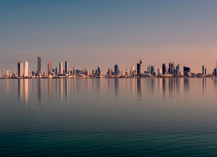 Beautiful Kuwait City skyline reflected on calm water at sunset, showcasing modern architecture.