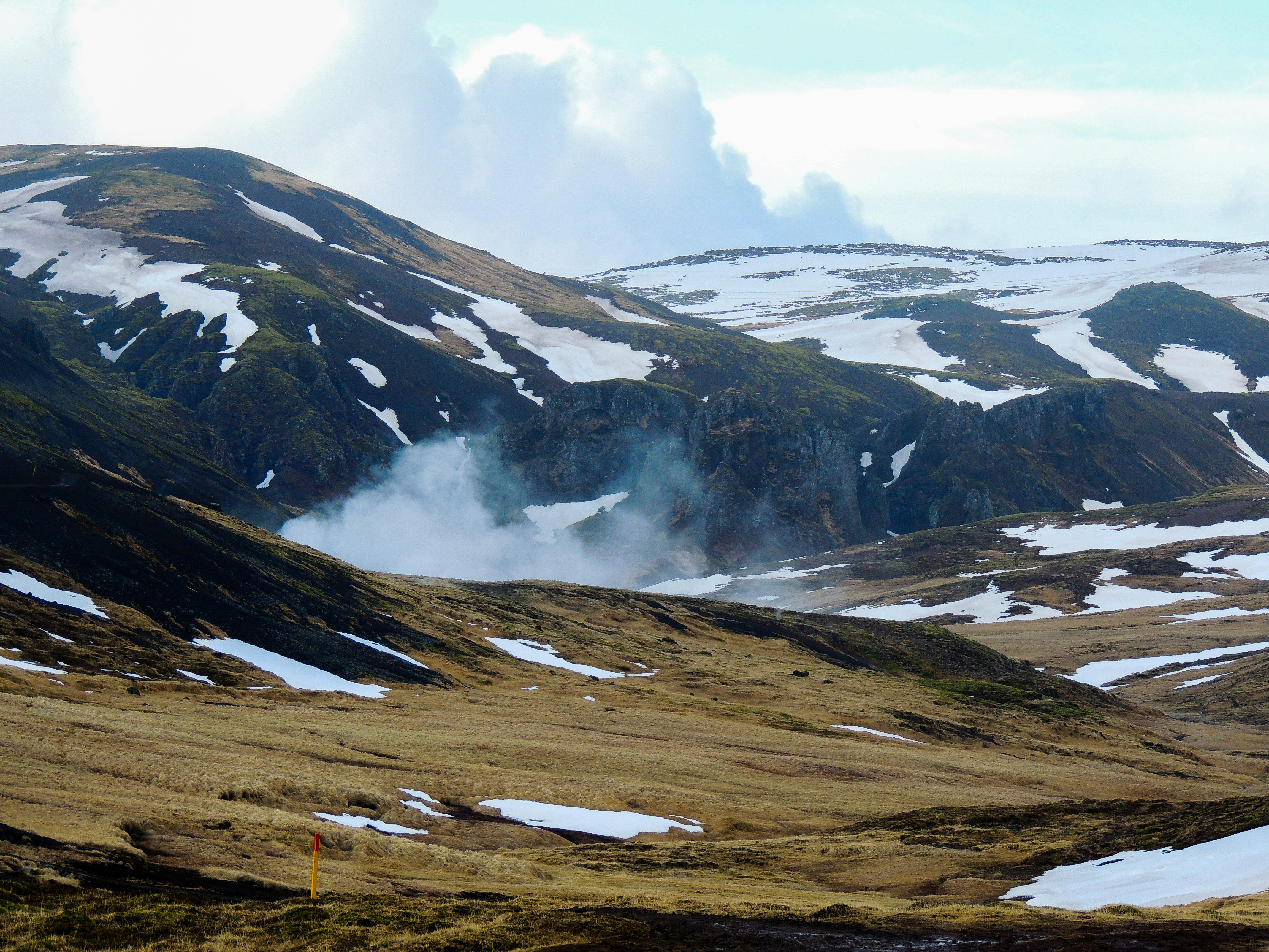 Majestic Icelandic highlands featuring snow-capped peaks and geothermal steam rising.