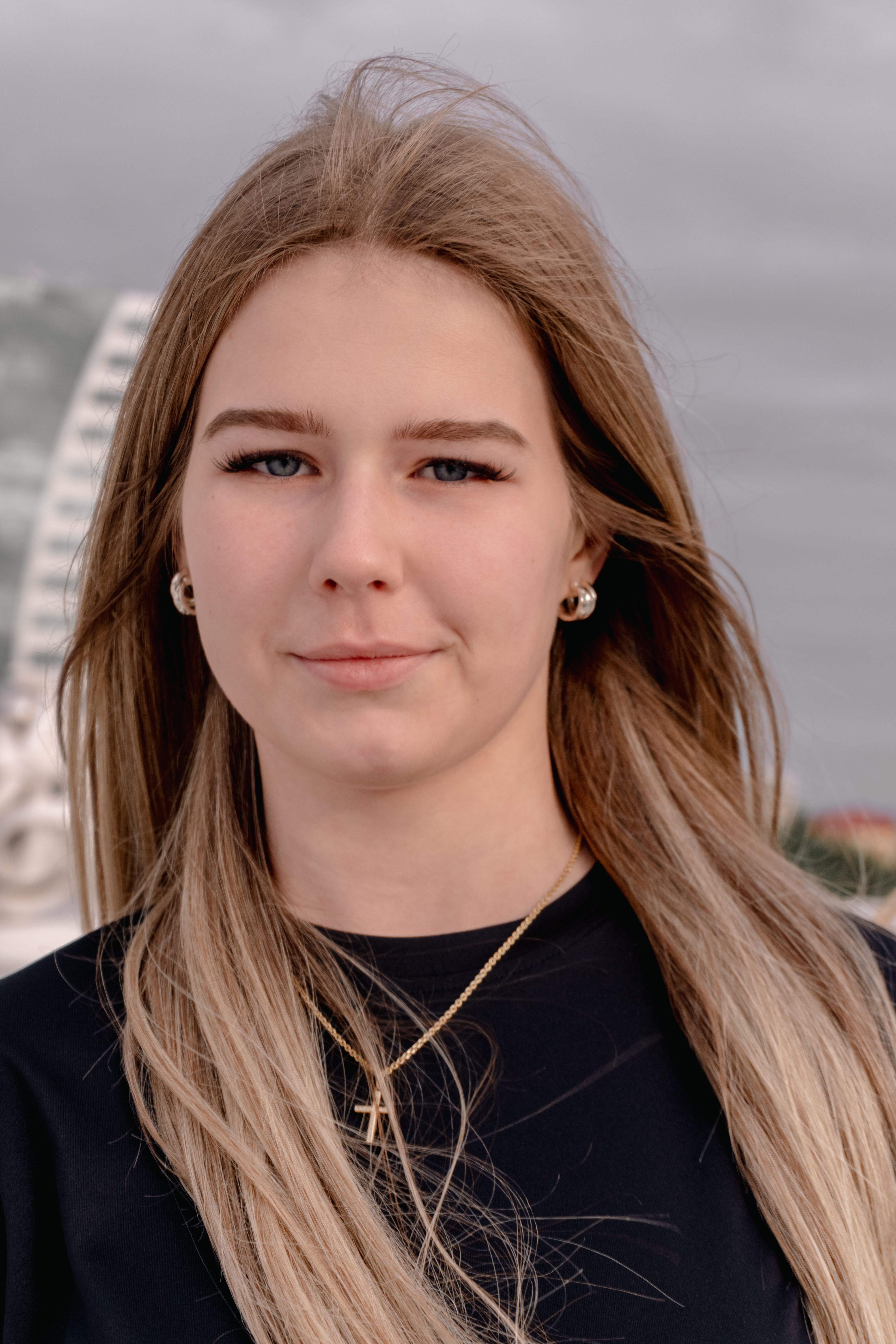 Close-up portrait of a young woman with long hair against an urban backdrop.