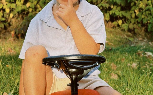 A toddler sitting on a red foot-to-floor ride-on car with a black steering wheel