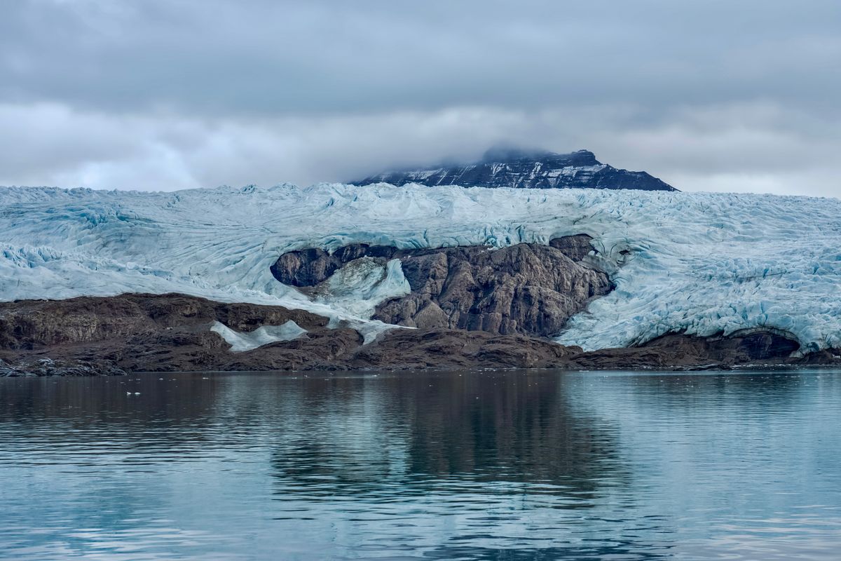 Nordenskiöldbreen's blue-white ice face dropping straight into the still water of Billefjorden, reflected below a low mountain.