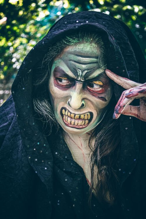 Free A person with dramatic witch makeup and a hooded cloak in an outdoor setting. Stock Photo