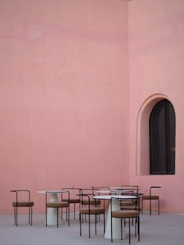 A stylish outdoor café with chairs and tables against a pink wall, capturing Doha's unique charm.