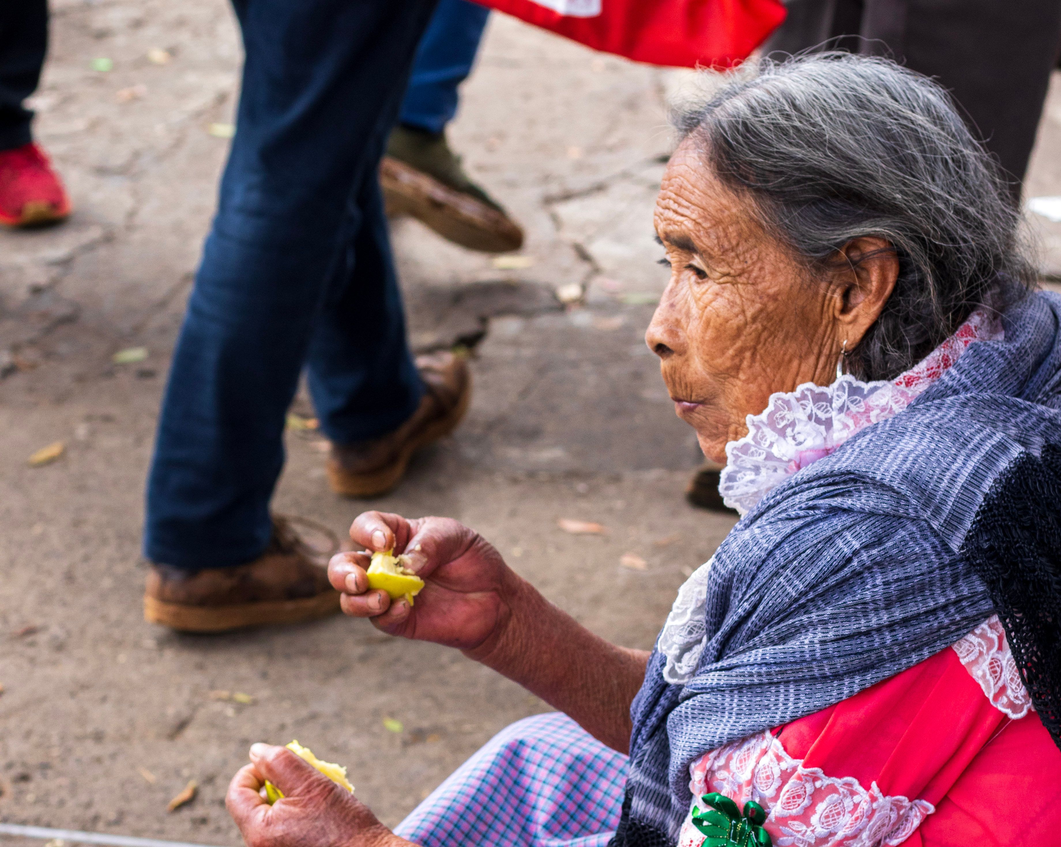Senior woman in traditional attire savoring fruit on a street in Michoacán, Mexico.