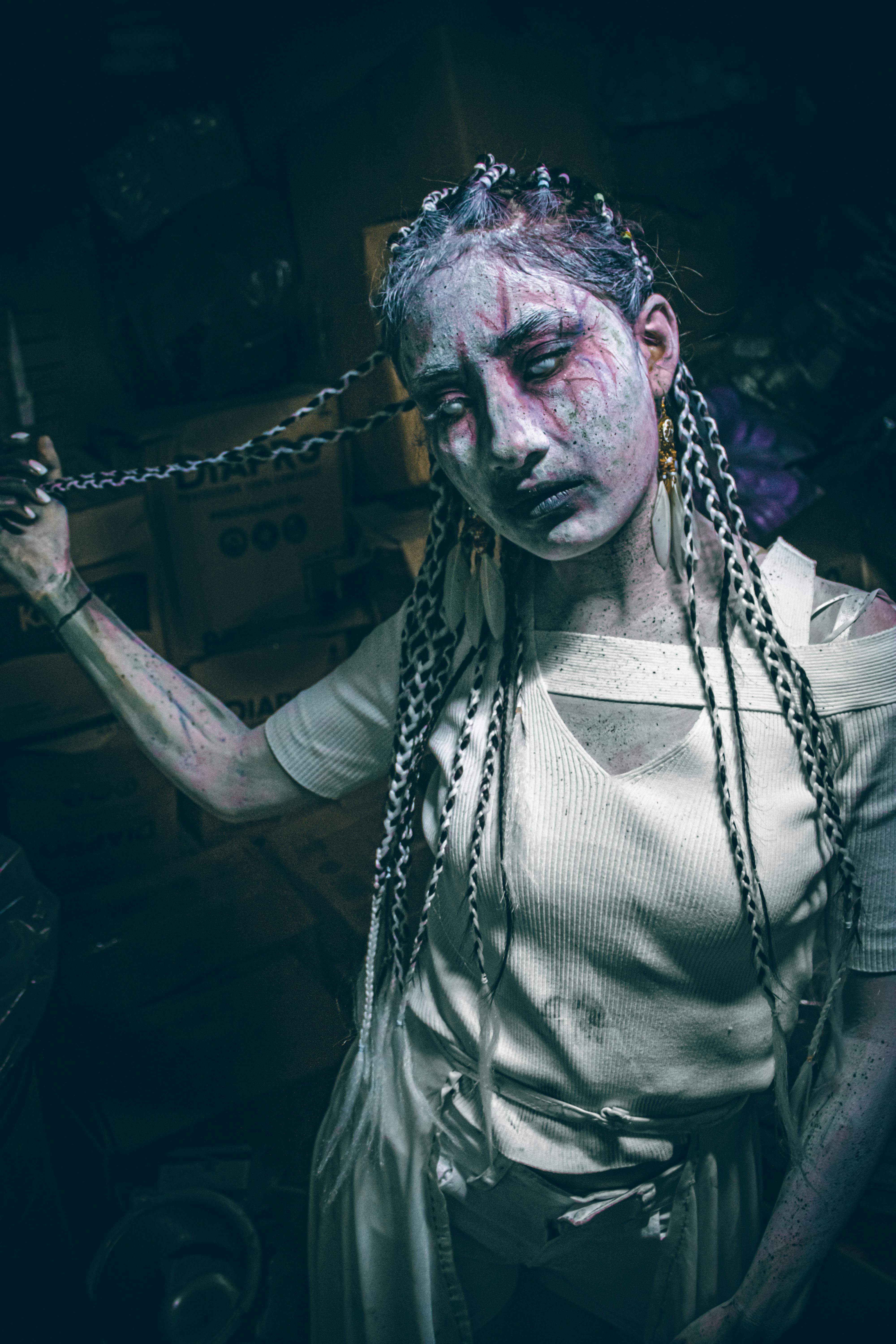 Ücretsiz Loş ışıklı bir odada elinde zincir tutan, sanatsal ve hayaletimsi makyajlı bir kişi. Stok Fotoğraflar
