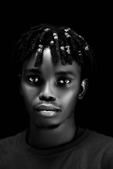 Striking black and white portrait of a young man with beads in his hair.