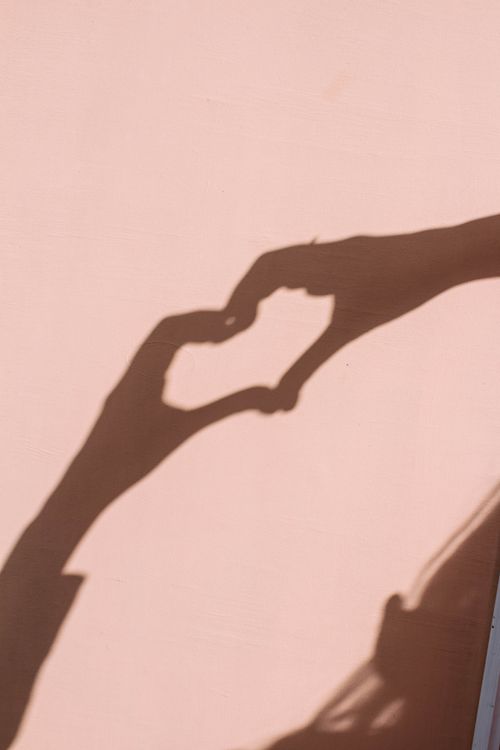 Free Shadow of a heart shape cast on a wall with a soft persimmon-colored background. Minimalistic and romantic image, perfect as wallpaper, background, or desktop screen Stock Photo