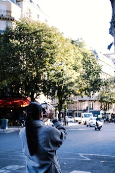 An adult woman photographs a bustling city street with her smartphone.