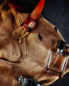 Stylish flat lay featuring a brown sweater, leather belt, wristwatch, and fragrance bottle.