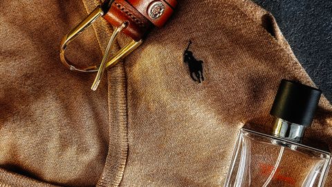 Stylish flat lay featuring a brown sweater, leather belt, wristwatch, and fragrance bottle.