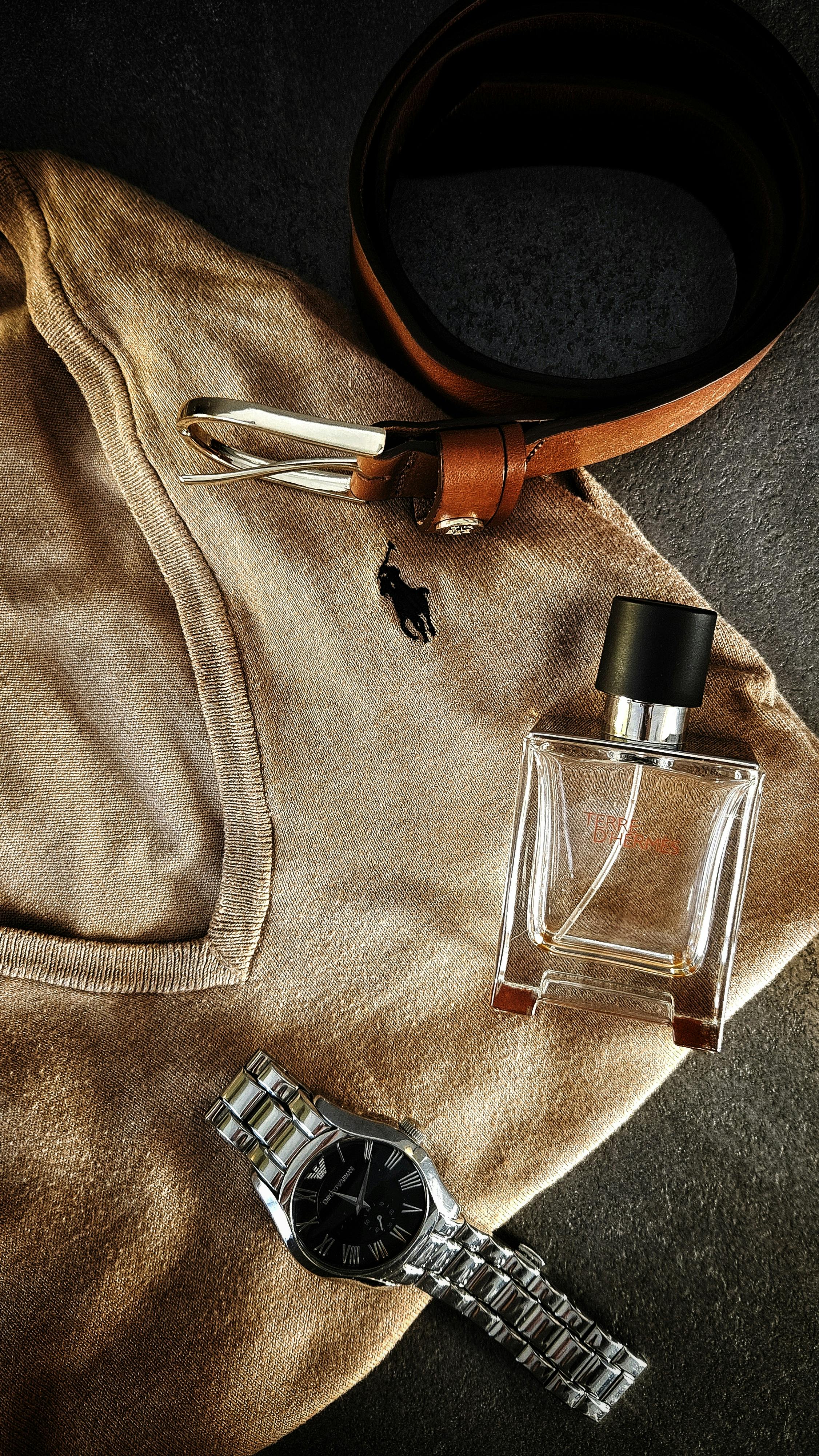 Stylish flat lay of brown sweater, belt, watch, and perfume for men's fashion inspiration.