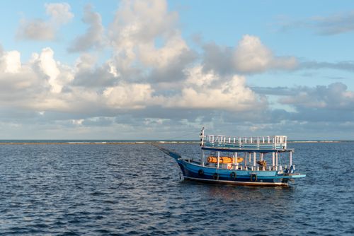 Free A serene blue boat floating under a sky with fluffy clouds in Arraial d'Ajuda, Brazil. Stock Photo