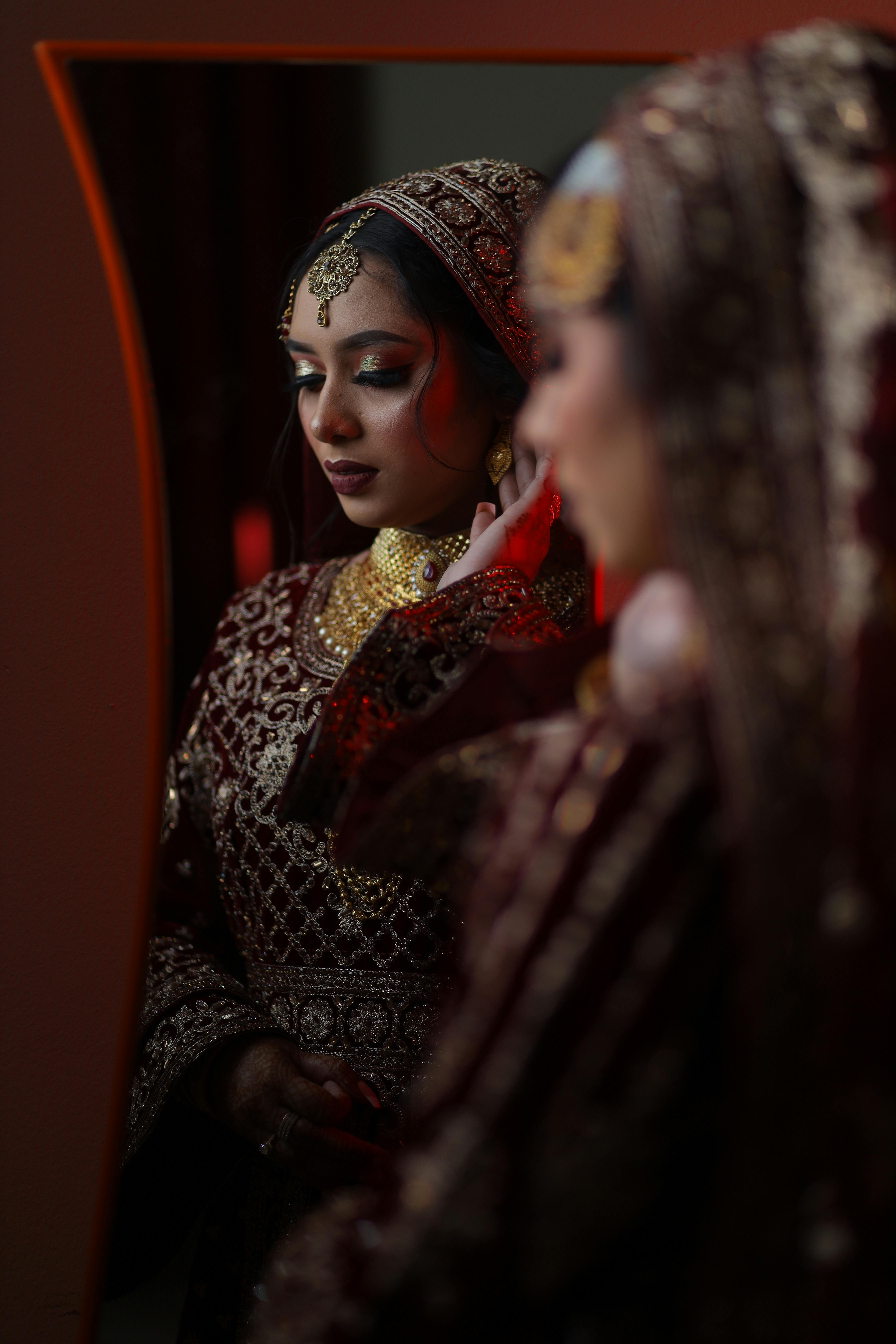 A beautiful South Asian bride in ornate attire gazing at her reflection, preparing for a wedding ceremony.