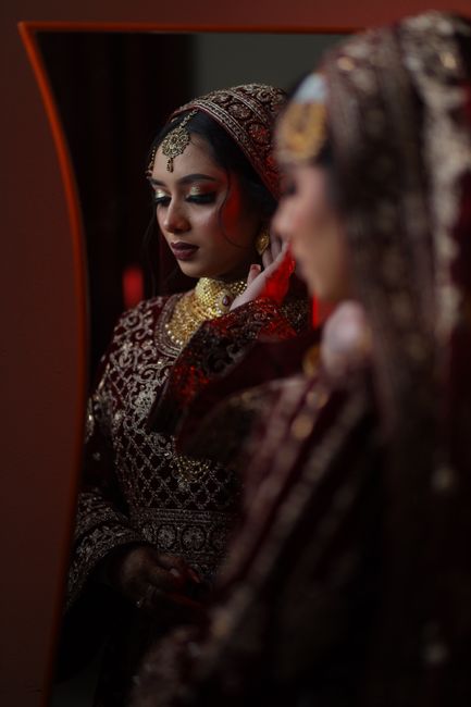 A beautiful South Asian bride in ornate attire gazing at her reflection, preparing for a wedding ceremony.