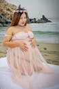 穿着粉色礼服、戴着花冠的孕妇坐在海滩上