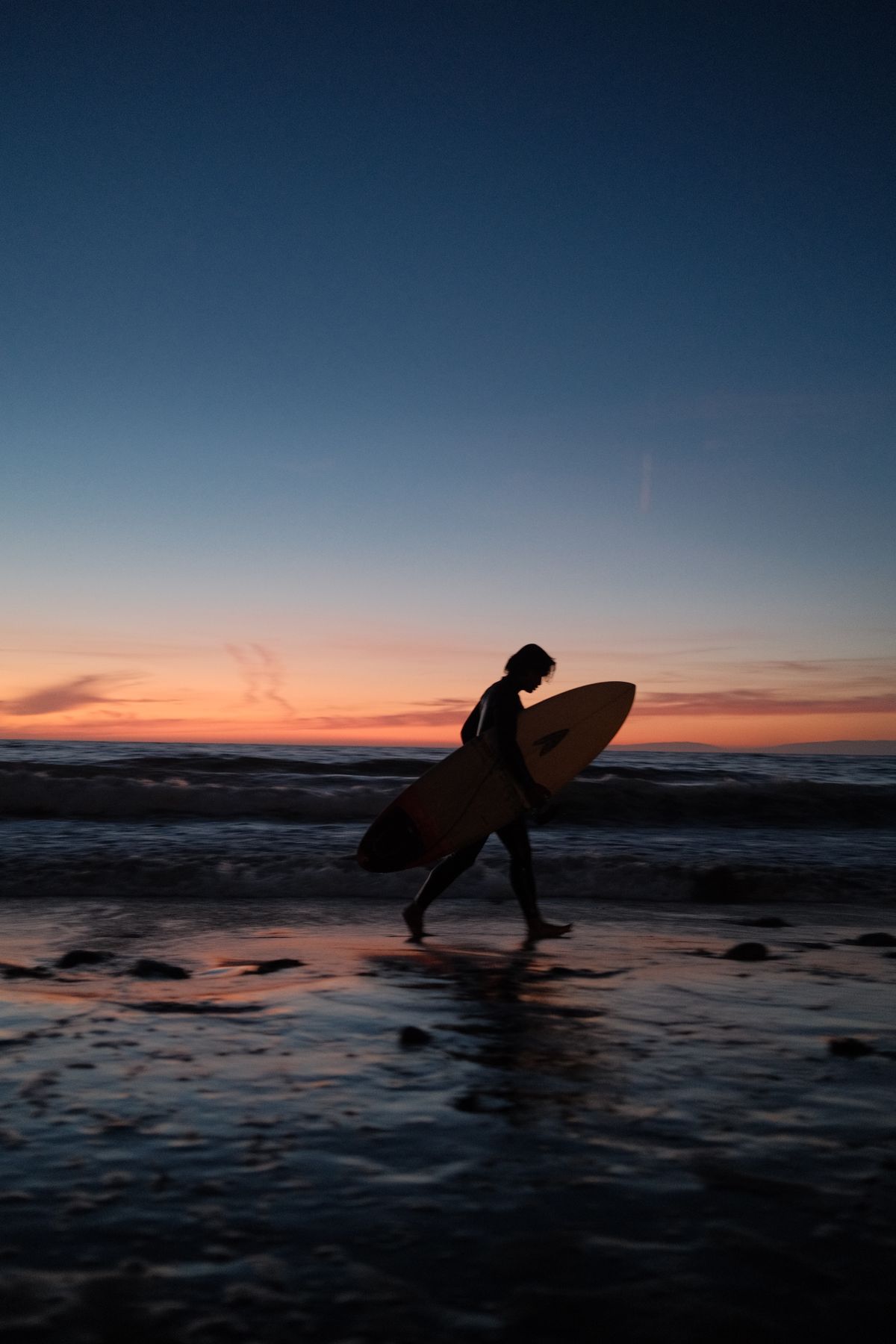 Solo surfer walking the beach at sunset with a surfboard