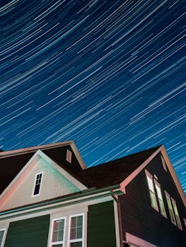 Vibrant star trails streak over a suburban house at night.